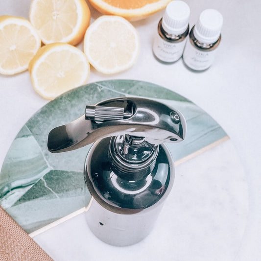 DIY cleaning spray. Dark bottle on a marble plate. Oranges and lemons cut. Two essential oil bottles and a tea towel. 